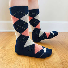 Load image into Gallery viewer, A child wearing a pair of navy blue and coral argyle socks on a wood floor