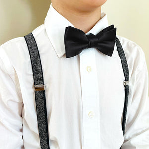 A child wearing a pair of black metallic suspenders with a black bow tie and white dress shirt