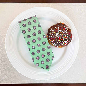 A mint green donut pattern tie displayed on a plate with a donut