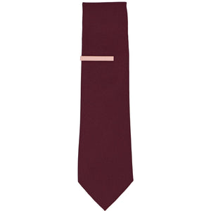 A solid blush pink tie bar on a dark burgundy necktie