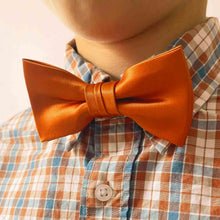 Load image into Gallery viewer, A child wearing a burnt orange solid bow tie with a burnt orange, blue and white checked shirt