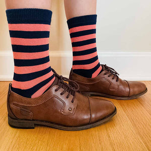 A child wearing a pair of coral and navy blue striped socks with brown dress shoes