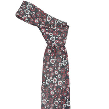 Load image into Gallery viewer, A patterned knotted necktie with a dark gray base and a dense floral print in crimson red, white, and black, styled in a knot on a plain white background.