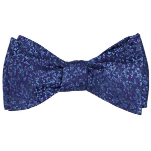 A dark purple and dark blue pebble pattern bow tie, tied