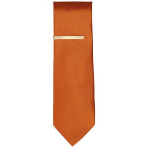 A gold tie bar on a burnt orange necktie