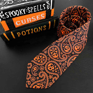 An orange and black skull and crossbones paisley tie in a loose roll with a stack of spell books