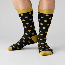 Load image into Gallery viewer, A pair of black crew socks with gold polka dots, gold ribbed cuffs, and gold toes, shown on a man's legs against a light gray studio background.