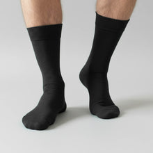 Load image into Gallery viewer, Man wearing black dress socks on a light gray background