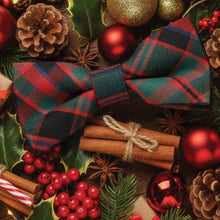 Load image into Gallery viewer, Red and green plaid bow tie surrounded by rustic Christmas decorations including red ornaments, pine cones, and cinnamon sticks.