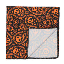 Load image into Gallery viewer, A black and orange skull and crossbones paisley pattern pocket square with the corner folded to show the backside