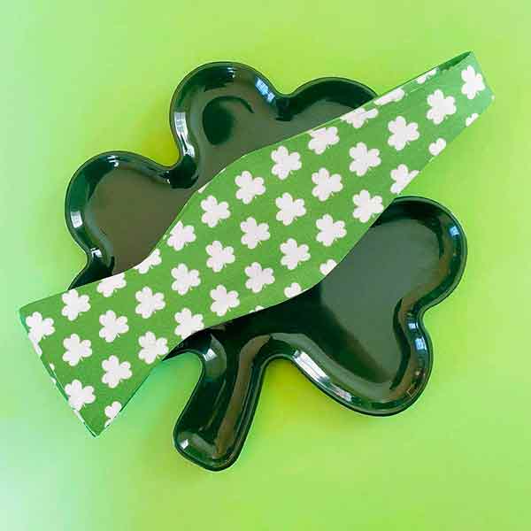 A green self-tie bow tie with white shamrocks on top of a green shamrock platter