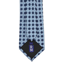 Load image into Gallery viewer, A steel blue necktie with a repeating navy blue geometric pattern, featuring a black silk tip with a RM crest logo.