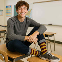 Load image into Gallery viewer, Teen boy in classroom wearing maroon and gold striped crew socks with rolled jeans and gray sneakers, sitting on a school desk and smiling.