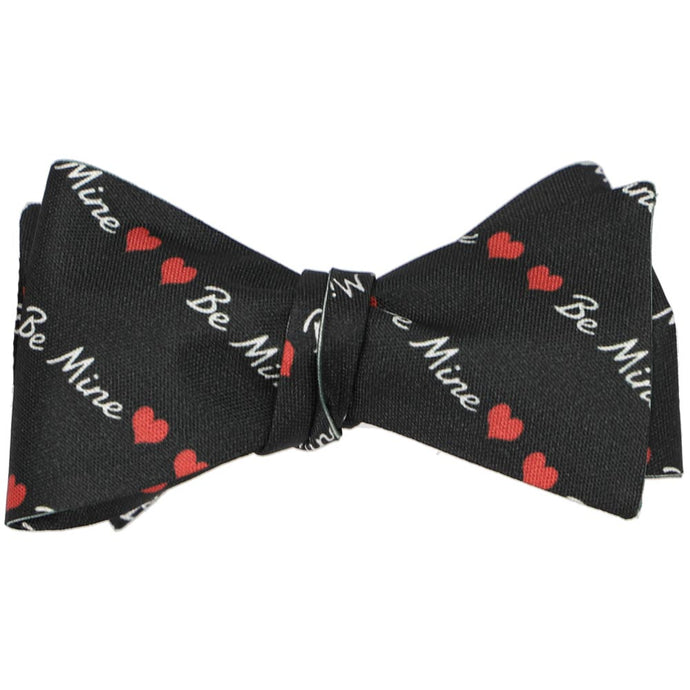 A black tied bow tie with a striped heart and be mine text pattern