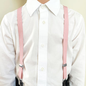 A boy wearing blush pink suspenders with a white dress shirt