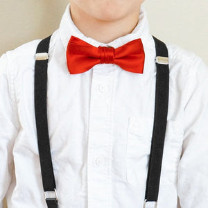 A boy wearing a pair of black suspenders with a red bow tie and white dress shirt