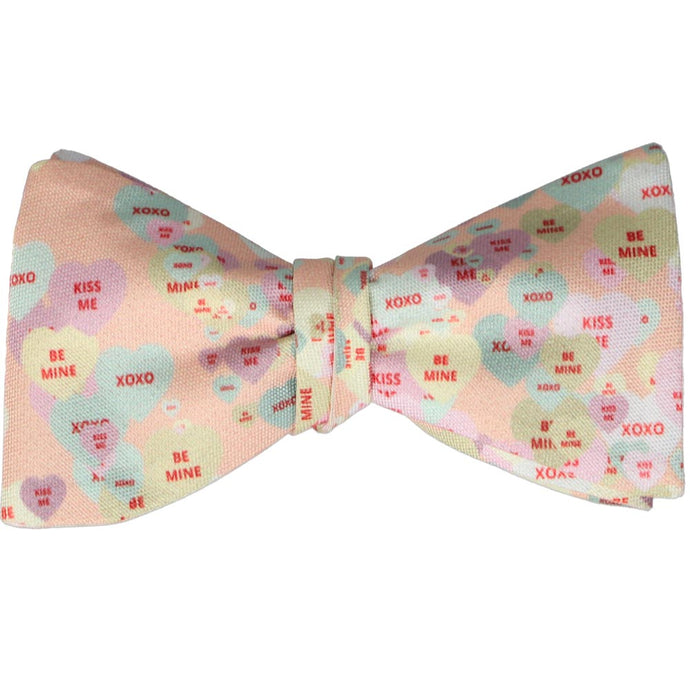 A tied self-tie bow tie with a candy hearts design in pastel shades