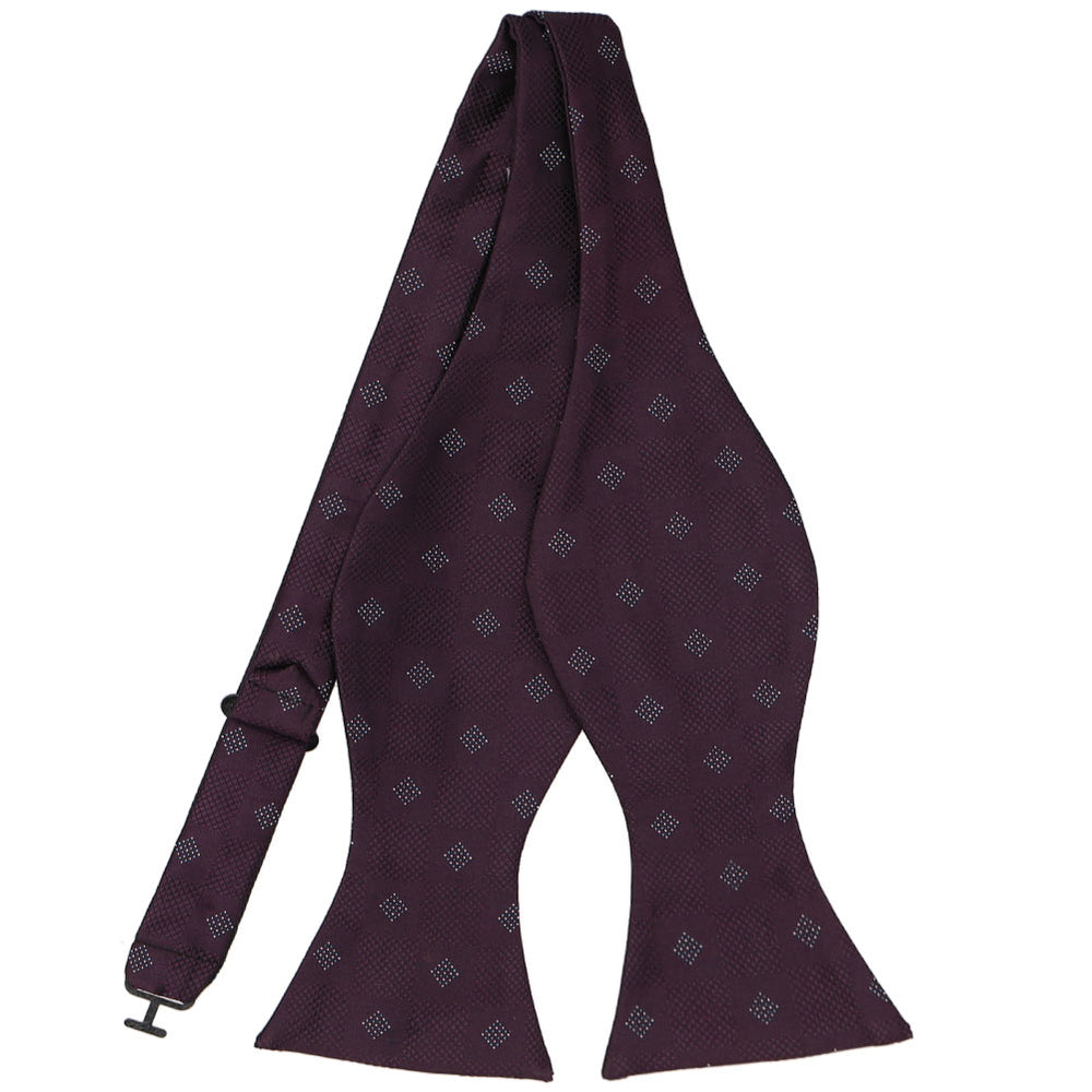 An untied self-tie bow tie in a dark eggplant color with a check pattern and textured details