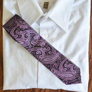 An eggplant purple slim tie displayed on top of a folded white dress shirt