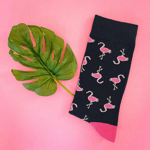 A folded navy and pink flamingo sock photographed next to a palm leaf on a pink background