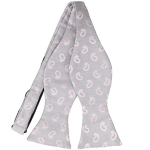 An untied light gray bow tie with a pink paisley design