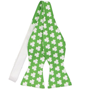 An untied self-tie bow tie in green with white repeating clovers