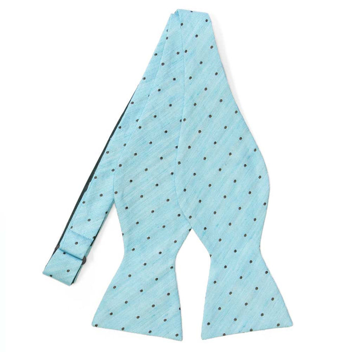 An untied light blue self-tie bow tie with small black dots