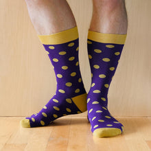 Load image into Gallery viewer, Closeup of a man wearing a pair of dark purple and gold polka dot socks standing on a wood floor