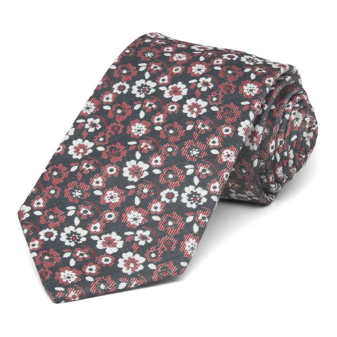 A crimson and white floral tie on a black background, rolled to show off the pattern