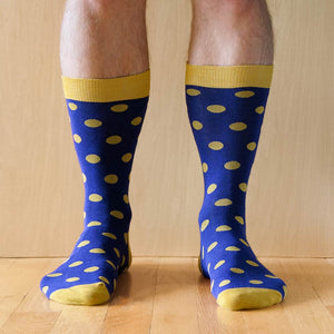 Man wearing a pair of royal blue and gold polka dot socks on wood floors