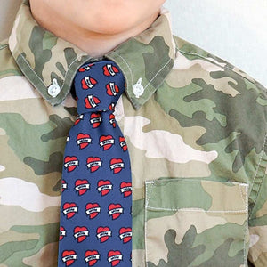 A boy wearing a camo button down shirt with a dark blue tie covered in mom heart tattoos