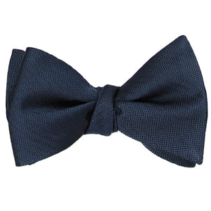 A tied navy blue silk self-tie bow tie in a tone on tone herringbone pattern