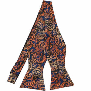 An untied self-tie bow tie with an orange ombre paisley pattern on top of a dark blue and black checked background