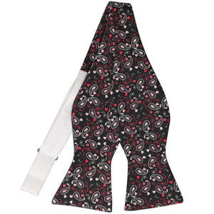 An untied black self-tie bow tie with pink and red paisley swirled with hearts