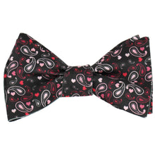 Load image into Gallery viewer, A tied black self-tie bow tie in a pink and red paisley heart pattern