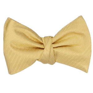 A self-tie bow tie, tied, in a pale gold herringbone pattern