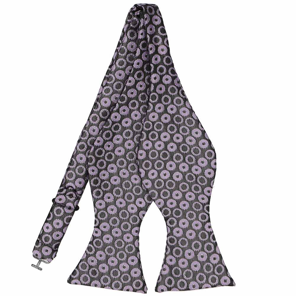 A purple and dark gray whimsical polka dot pattern self-tie bow tie. The polka dots have large and small gray dots in the middle.