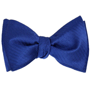 A sapphire blue herringbone self-tie bow tie, tied